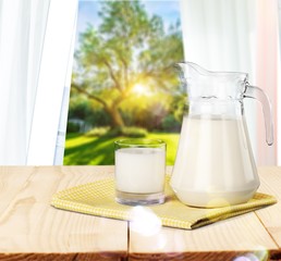 Glass and jug of milk with green meadow on background