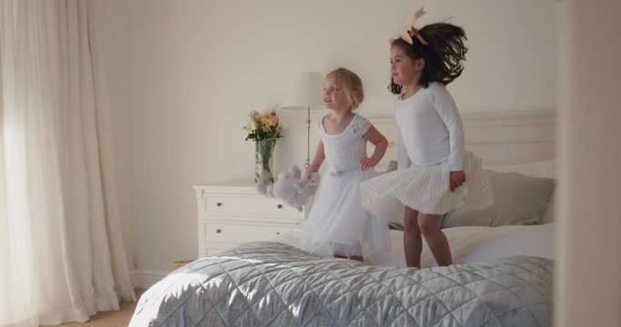 happy little girls playfully jumping on bed sisters having fun children in playful mood wearing pretty dresses 4k