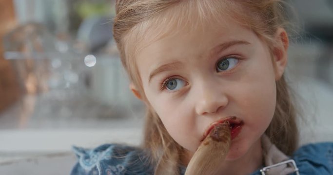 happy little girl licking spoon tasting delicious chocolate pudding enjoying homemade treats in kitchen 4k