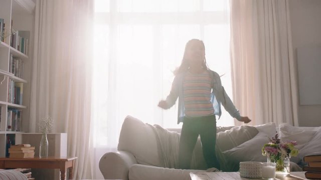 Happy Little Girl Jumping On Sofa Dancing Having Fun Child In Playful Mood Enjoying Weekend Morning At Home With Sunlight Shining Through Window 4k Footage