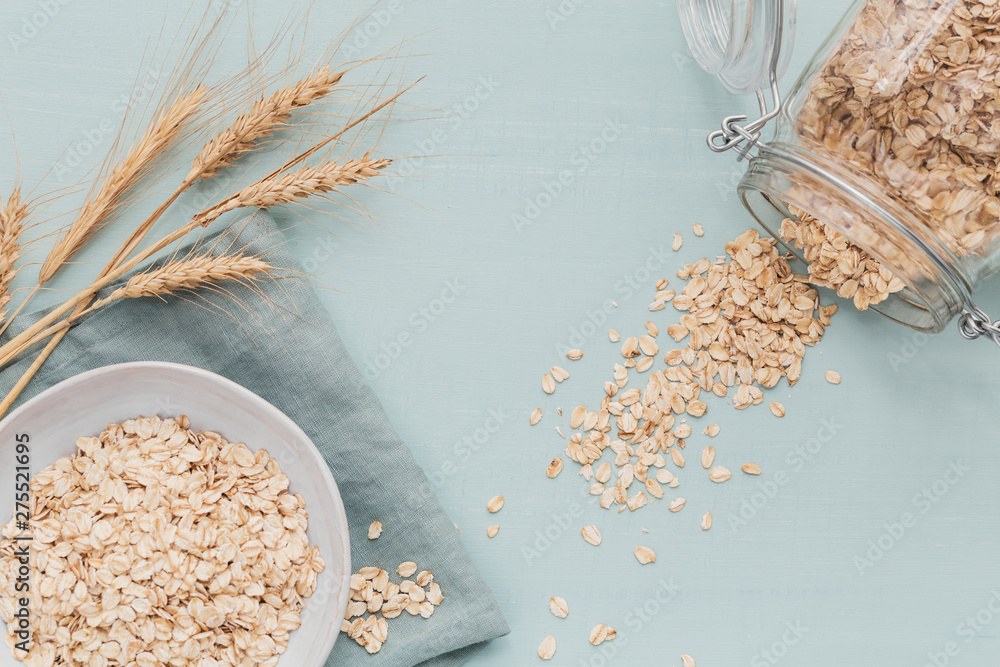 Wall mural bowl of dry oat flakes with ears of wheat on light background. cooking oats porridge concept