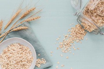 Fototapeta bowl of dry oat flakes with ears of wheat on light background. Cooking oats porridge concept obraz