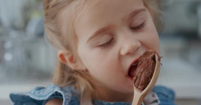 happy little girl licking spoon tasting delicious chocolate pudding enjoying homemade treats in kitchen 4k