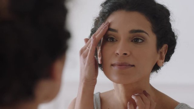 portrait beautiful young woman looking in mirror at perfect healthy skin touching face with hands enjoying smooth natural complexion with anti aging skincare getting ready at home beauty concept