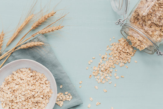 bowl of dry oat flakes with ears of wheat on light background. Cooking oats porridge concept