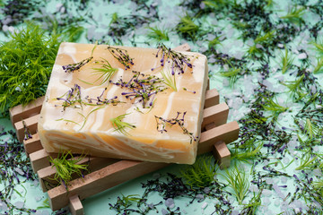 Wooden Soap Holder with Handmade ultra-moisturizing Almond Scented Goats Milk Bar Soap decorated with flower sprinkles confetti on green background.