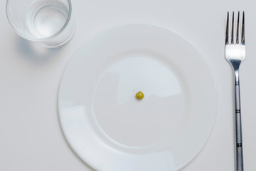 diet concept. one pea on an empty white plate with fork