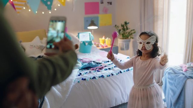 happy little girl playing dress up in bedroom with mother taking photo using smartphone sharing on social media