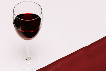 A glass of cherry wine on a red and white background and cherry berries.
