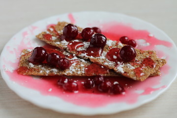 dessert with red berries, poured with cherry jam with powdered sugar on a white plate, on a wooden table, closeup