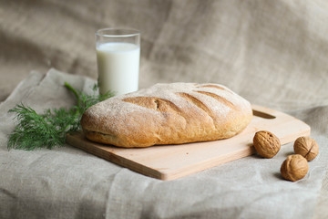 freshly baked bread with milk in a glass with walnuts and dill on a wooden board on a linen background, closeup
