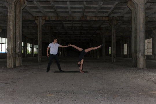 A young girl and boy perform acrobatic moves in the premises of an old factory, a warehouse, acro 