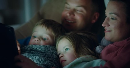 happy family using tablet computer with children mother and father enjoying watching entertainment with kids on touchscreen technology relaxing before bedtime  - Powered by Adobe