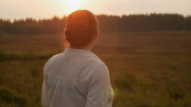 girl standing in a field at sunset brushing off mosquitoes