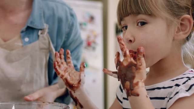 happy little girl with hands covered in chocolate licking fingers having fun baking in kitchen naughty child playing enjoying childhood