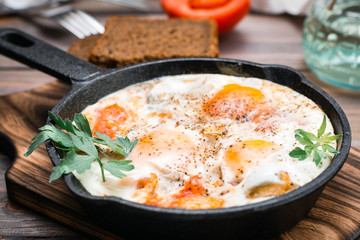 Ready-to-eat shakshuka from fried eggs with tomatoes and parsley in a pan on a wooden table