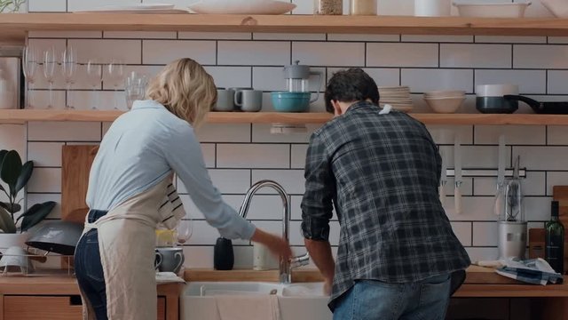 happy young couple washing dishes playing in kitchen having fun throwing soap bubbles enjoying romantic relationship playfully doing household chores 4k footage