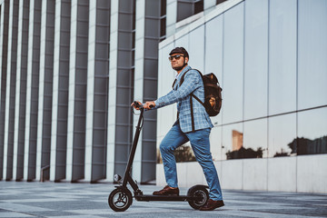 Cheerful modern man is driving his electro scooter near his office after long hard day. © Fxquadro