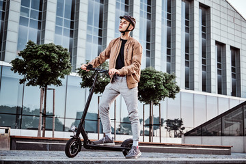 Young attractive student is driving his scooter neat interesting glass building at bright sunny day. © Fxquadro