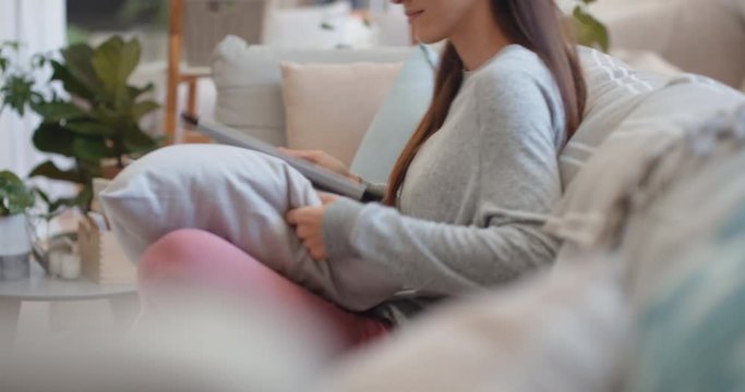 young woman using tablet computer browsing online scrolling looking at social media pictures with mobile touchscreen technology relaxing on sofa at home 4k
