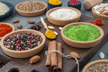 Spices lie in bowls and wooden spoons on a gray background , top view, soft focus. Spices and seasonings for cooking in the composition on the table.