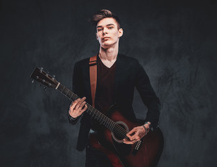 Obraz premium Young attractive man is playing acoustic guitar at studio while posing for photographer.