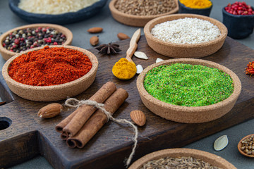 Spices lie in bowls and wooden spoons on a gray background , top view, soft focus. Spices and seasonings for cooking in the composition on the table.