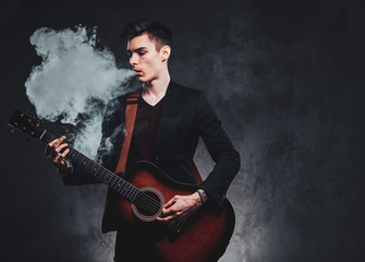Fototapeta na wymiar Young attractive man is playing acoustic guitar while smoking vape, making big haze.