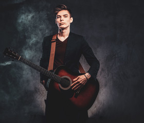 Young attractive man is playing acoustic guitar at studio while posing for photographer.