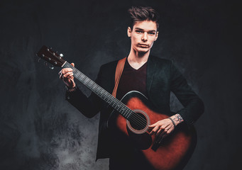 Portrait of handsome young man at studio with acoustic guitar in hands on the dark background.