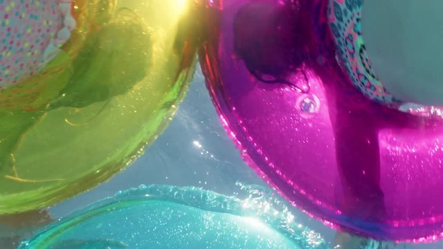 children swimming in pool with colorful swim tube inflatable toys splashing playfully having fun together on water floats enjoying summer vacation underwater view