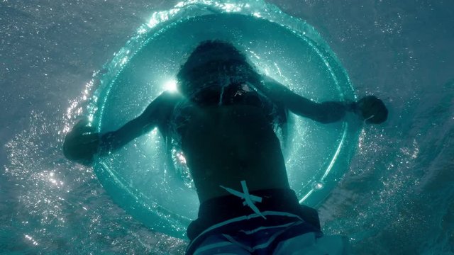 underwater view little boy swimming in pool with colorful swim ring inflatable toy kid splashing playfully having fun on water floats enjoying summer day pov 4k