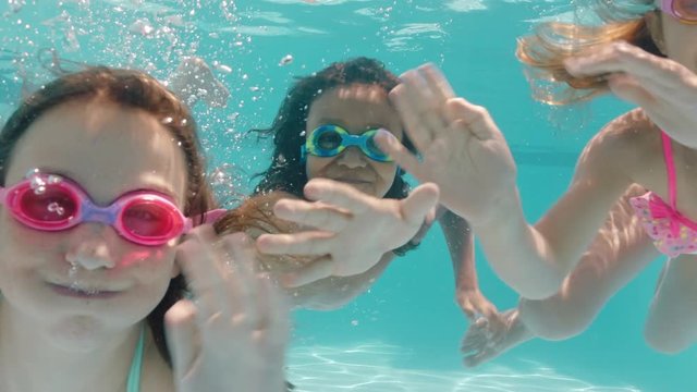 happy children swimming underwater in pool smiling waving hands kids enjoying swim floating together in crystal clear water on summer vacation