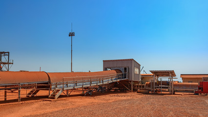 Covered conveyor belt mechanism transports bauxite ore, which is refined into aluminum, from an storage outside area to transhipment into a capesize bulk carrier ships in the Kamsar, Guinea, Africa.