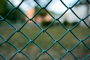 Closeup photo of a green iron fence. Only the links of the grid in focus.