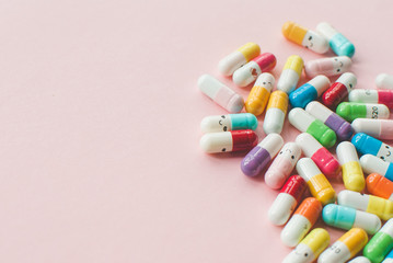 Pile of colored capsule and tablets on a pastel pink background