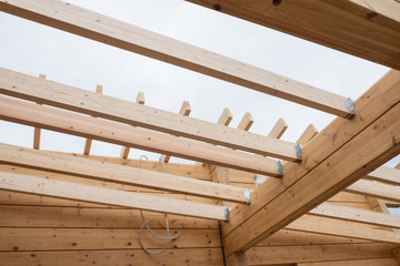 Details of a wooden house. The beams of the ceiling and the walls of the house of glued laminated timber. Summer day.