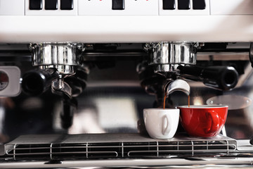 Aromatic coffee pouring into cups from modern machine, closeup