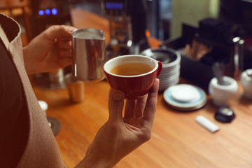 Barista holding cup of coffee and jug with milk at bar counter, closeup. Space for text