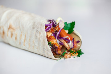 Shawarma sandwich - fresh roll of thin lavash (pita bread) filled with grilled meat, mushrooms, cheese, cabbage, carrots, sauce, green. Traditional Eastern snack. On a wooden background