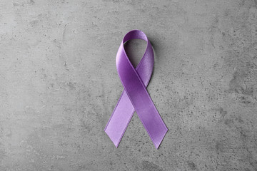 Purple ribbon on grey stone background, top view. Domestic violence awareness