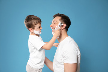 Obraz na płótnie Canvas Little son shaving his dad on color background
