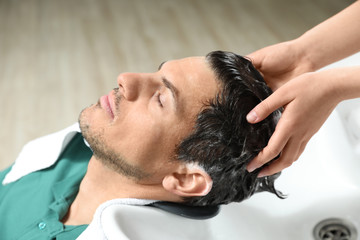 Fototapeta premium Stylist washing client's hair at sink in beauty salon