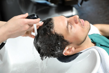 Stylist washing client's hair at sink in beauty salon