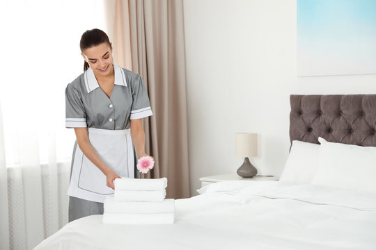 Chambermaid putting flower on fresh towels in hotel room. Space for text