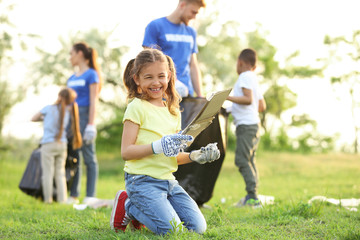 Little girl collecting trash in park. Volunteer project