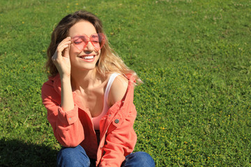 Portrait of happy woman with heart shaped glasses on green lawn