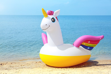 Funny inflatable unicorn ring on sandy beach near sea. Space for text © New Africa