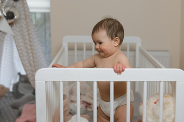 Baby girl in a diaper playing in the crib.
