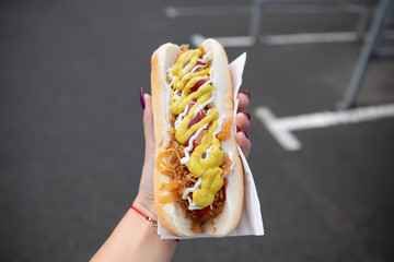 A young woman holds a bitten hot dog in her hand. Snack in the parking lot near the shopping center.